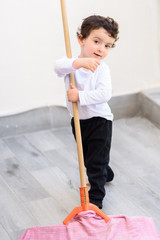 Portrait of little smiling boy cleaning tile floor with mop and rag.