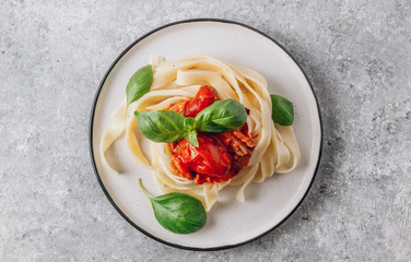Pasta Tagliatelle Bolognese with meat tomato sauce and fresh basil leaves on white plate. Light gray table. Top view