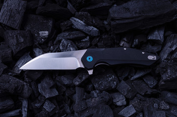 Pocket knife lying on cold coals. Top view of a knife and coal.