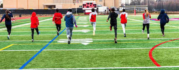 Track runners doing warm up running drills on turf field