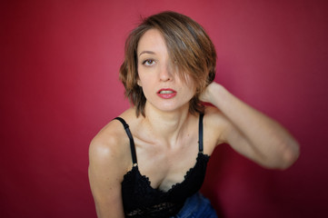 Fototapeta premium Young woman with short hair dressed in black lace bustier and blue jeans is posing in the studio on bright pink background