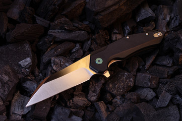 A sharp pocket knife lies at an angle on the coals.