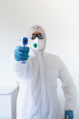 Doctor holding infrared thermometer. Portrait of medical professional in protective clothing measuring contactless fever at Covid-19 test center during coronavirus epidemic.