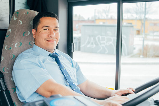 young smiling hispanic bus driver is holding a wheel, looking at the road.