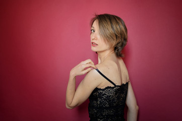 Young woman with short hair dressed in black lace bustier and blue jeans is posing in the studio on bright pink background