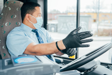 young man bus driver puts black  gloves on his hands to protect himself from the coronavirus