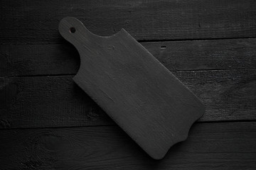 Black chopping board on painted dark black wooden deck background, with copyspace for text