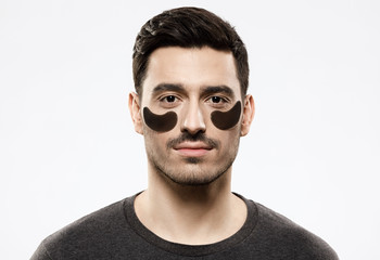 Portrait of young male in t-shirt with black gel patches attached under eyes, willing to hide skin...