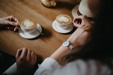 hands of man an woman sitting in cafe with coffee with hearts