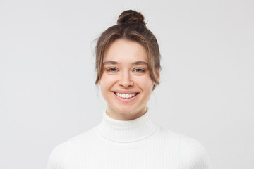 Close-up portrait of young pretty female looking at camera with happy smile, hair tied in bun with...