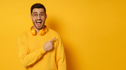 Horizontal banner of surprised man feeling shocked about beneficial commercial offer, pointing to copy space on right, screaming WOW, isolated on yellow background
