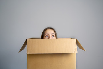 Think outside the box concept. Funny girl with scared face looking out of box at grey background....