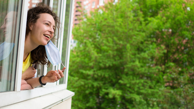 Quarantine is over concept. Woman taking off medical mask looking out of window 