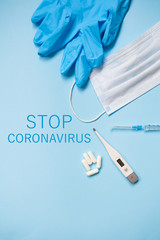 Disposable medical mask, blue gloves with pills, syringe and thermometer on a blue background.