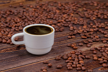 Cup of coffee and scattered coffee beans on the table. Rustic wooden surface.