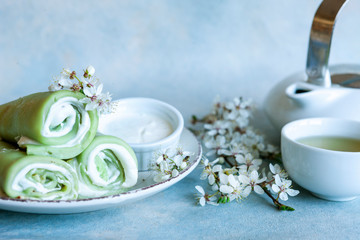 Delicious homemade green pancakes with blossoming cherry tree branches with green  tea on sky blue background.