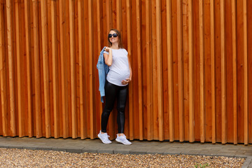 Smiling thirty-year pregnant woman in white T-shirt and white sneakers