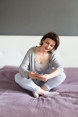 Young happy woman in grey relaxing at home, texting and chatting at her mobile phone.