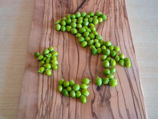 Italy shape made out of fresh green peas on top of a wooden cutting board. Italy food map