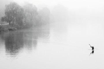 Obraz na płótnie Canvas Man on kayak in fog. Misty river. Black white autumn landscape