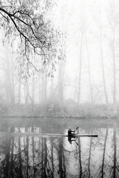 Man on kayak in fog. Boat on autumn river. Black white photo
