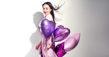 Valentine Beauty girl with colorful heart air balloons laughing, isolated on white background. Beautiful Happy Young woman. Holiday birthday party,  having fun, celebrating with pink color balloon. 