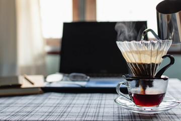 Close Up drip coffee maker with hot smoke in stainless pot, Morning coffee time with notebook computer and work equipment, Normal practice by working at home during covid-19 outbreak around the world.