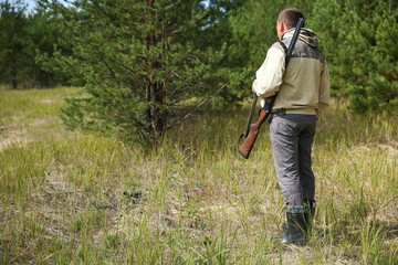 standing hunter with rifle in summer forest