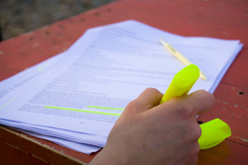 Female hand holding highlighter pen, highlighting / marking important texts in study sheets on...
