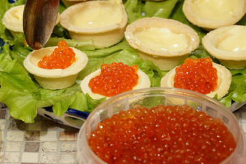    Unfolding red caviar in tartlets with butter, which lie on a plate with lettuce.