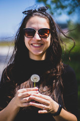 Obraz premium Caucasian girl smiling with a dandelion in a cloudy bright day in front view. Concept: Carefree happiness