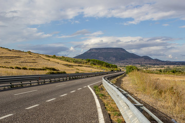  Sunny sky with clouds and beautiful asphalt road with crash barrier.  Green hills,  fields with grass. Beautiful landscape in Sardinia in summer, Italy.