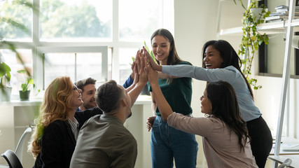 Funny diverse workers with happy female leader, coach giving high five at company meeting. Smiling...