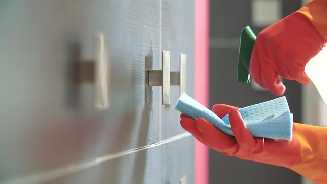 Nettoyage par d&eacute;sinfection du coronavirus en pulv&eacute;risant un antisepsie assainissent sur une poign&eacute;e de porte de placard m&eacute;tallique, muni de gant de protection.