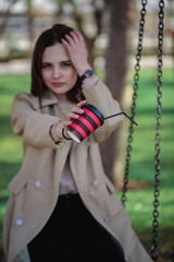 Portrait of a girl with a blurred face, holding a red-black glass with a straw in front of her hands. A disposable glass with a drink in female hands.