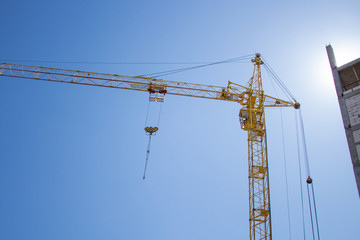 A crane at a construction site is building a tall house. Against the background of blue sky and bright sun.copyspace for text.