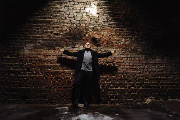 Young man in the coat standing near the wall with arms wide apart