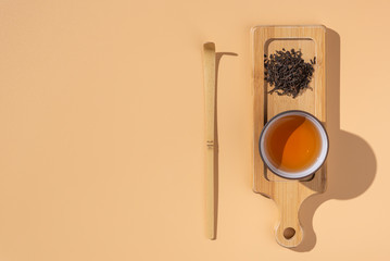 Ceramic cup with black puer tea ,dry pu-erh tea leaves in a wooden bamboo plate on a beige background, tea ceremony,minimalism style.