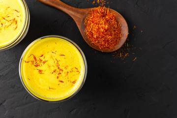 Latte Saffron a glass cup on a black concrete background, wooden spoon with dry spice saffron,golden milk,top view,copy space