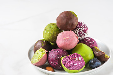 Healthy vegan dessert food. Raw colorful energy balls in chocolate glaze in a plate on white table