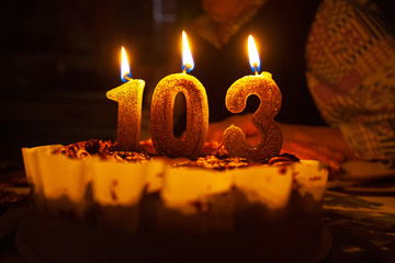 Grandmother's birthday, 103 years. On the table is a birthday cake with candles. Dark background....