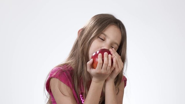 Little girl on white eats a big red apple. A girl bites a piece of red ash and tastes it.