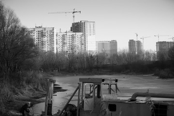 The evening of a winter day. Large houses on the background of a frozen lake. An old dredger in the foreground. Horizontal frame. Soft focus