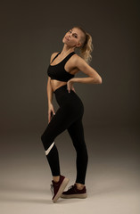 Happy young woman in sports clothing smiling. Muscular fitness model on grey background looking away at copy space. Trained body.