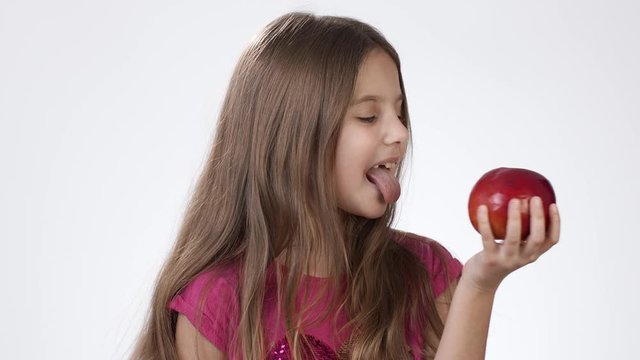 Little girl on white eats a big red apple. A girl bites a piece of red ash and tastes it.