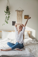 beautiful young blonde girl sitting on a bed in a light bedroom and stretching