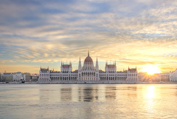 Fototapeta na wymiar Hungarian Parliament at sunrise across the Danube in Budapest with colorful cloudy sky and sun rays