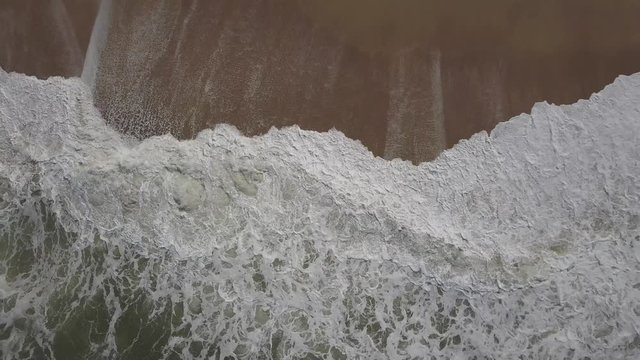 Flying over a sandy beach. Waves break on a sandy beach on the Atlantic coast, aerial View. Nazare, Portugal. (raw video).