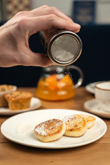 Man sprinkles powdered sugar on cottage cheese pancakes.