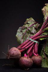 Couple of rough textured purplish matt red beet still on stems with leaves behind contrasted...